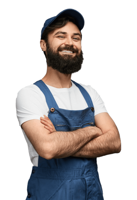 A smiling man with a beard wearing a cap and blue overalls with his arms crossed.